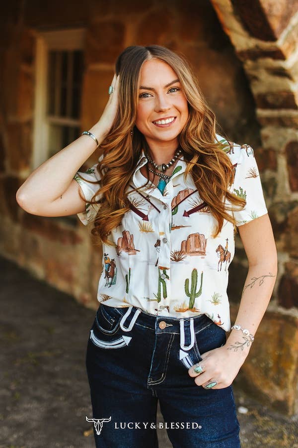 Women's white Texas western pearl snap shirt featuring an all over desert cactus and cowboy print styled with dark denim jeans.