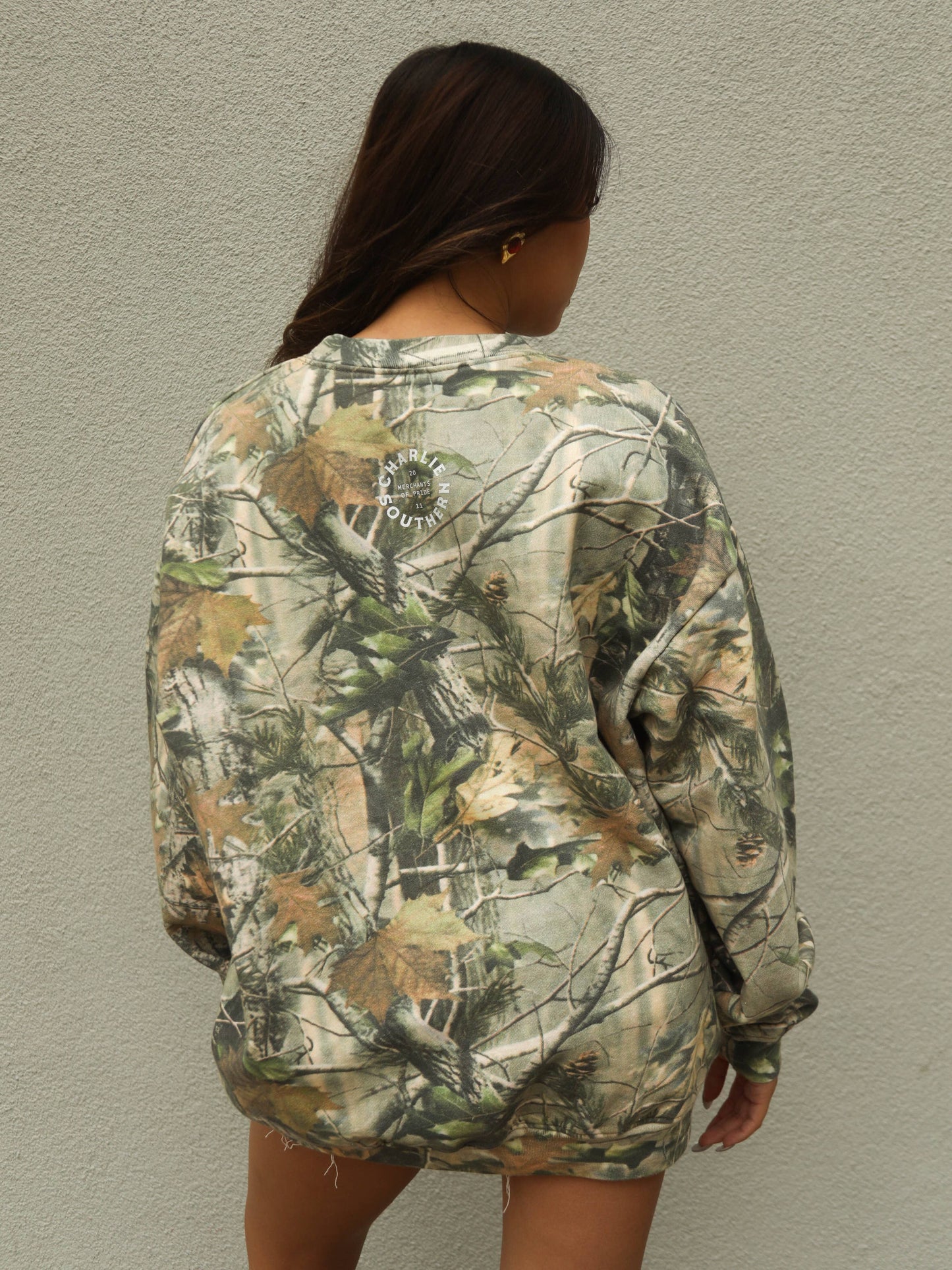 Country inspired oversized sweatshirt with hunting camo print, rodeo graphic design and relaxed styling paired perfectly with denim shorts, trucker cap and cowboy boots
