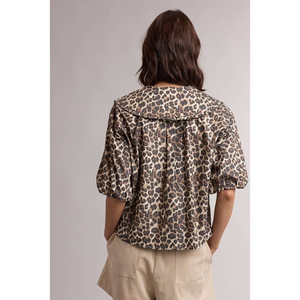 Person wearing a leopard print jacket and beige pants on a plain background