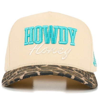 Front view of full-cotton trucker cap featuring turquoise embroidered “Howdy” and off-white embroidered “Honey” lettering across the cream crown, a black and white cow print curved brim, and playful western-inspired country styling.
