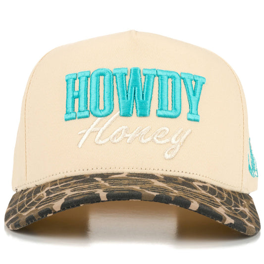 Front view of full-cotton trucker cap featuring turquoise embroidered “Howdy” and off-white embroidered “Honey” lettering across the cream crown, a black and white cow print curved brim, and playful western-inspired country styling.
