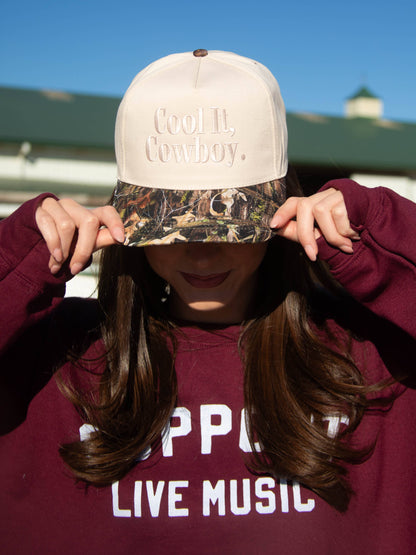 Cream and camo trucker cap with "Cool It, Cowboy" embroidered on the front