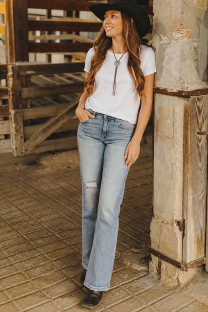 Light wash western flare jeans with distressed knee detailing and flattering high-rise fit styled with a white tee and cowboy boots.