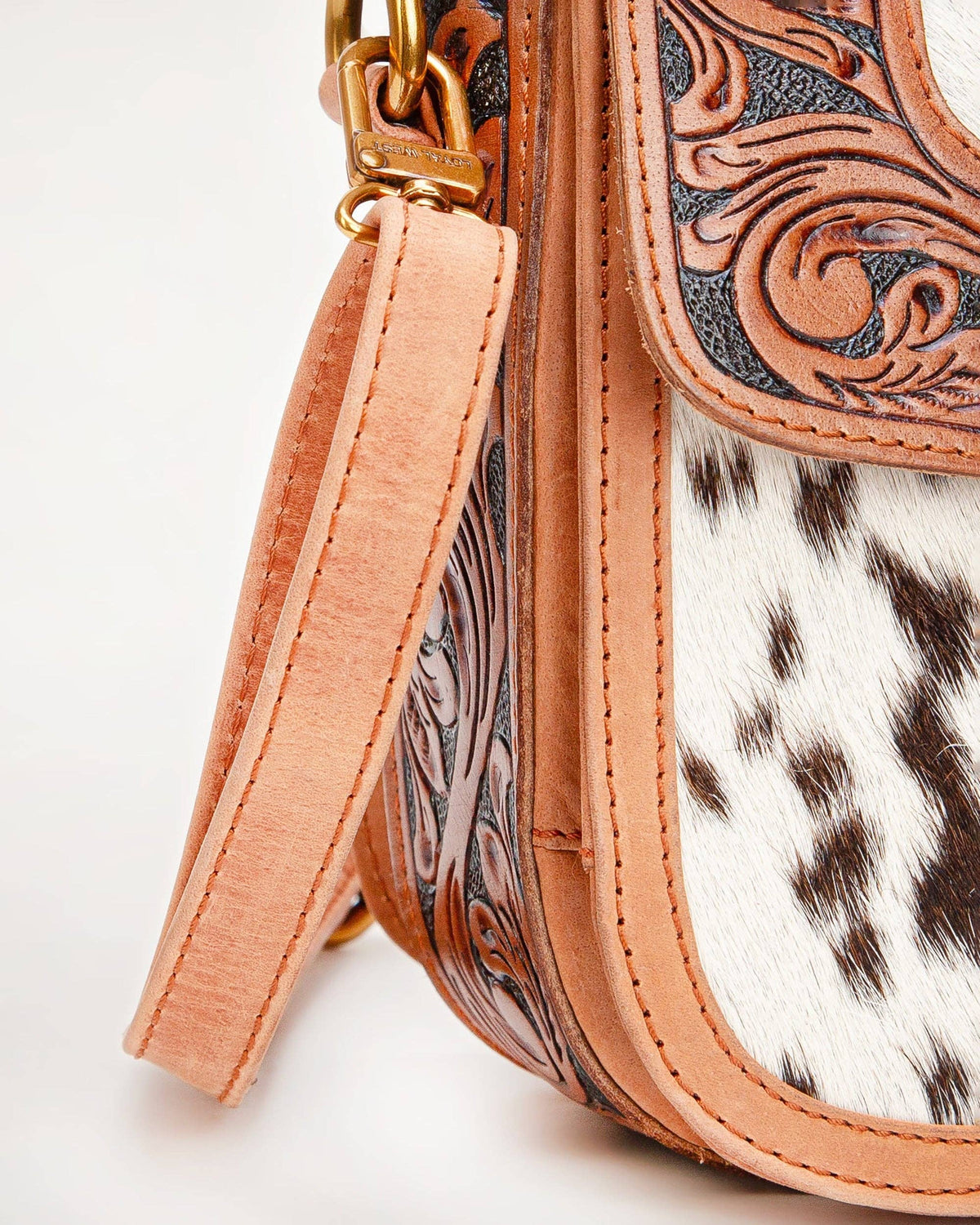 Close-up of a handbag with cowhide leather and intricate tooled design on a light background