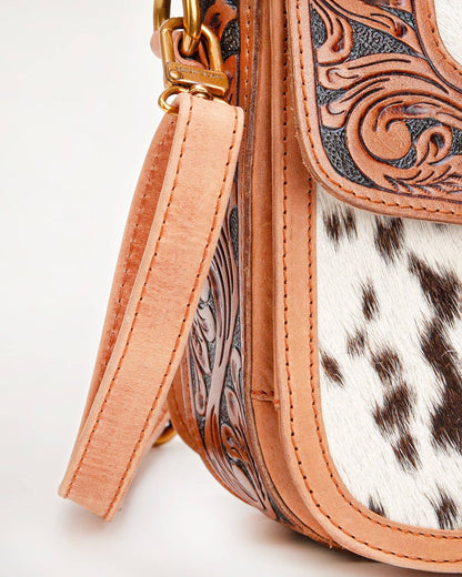 Close-up of a handbag with cowhide leather and intricate tooled design on a light background