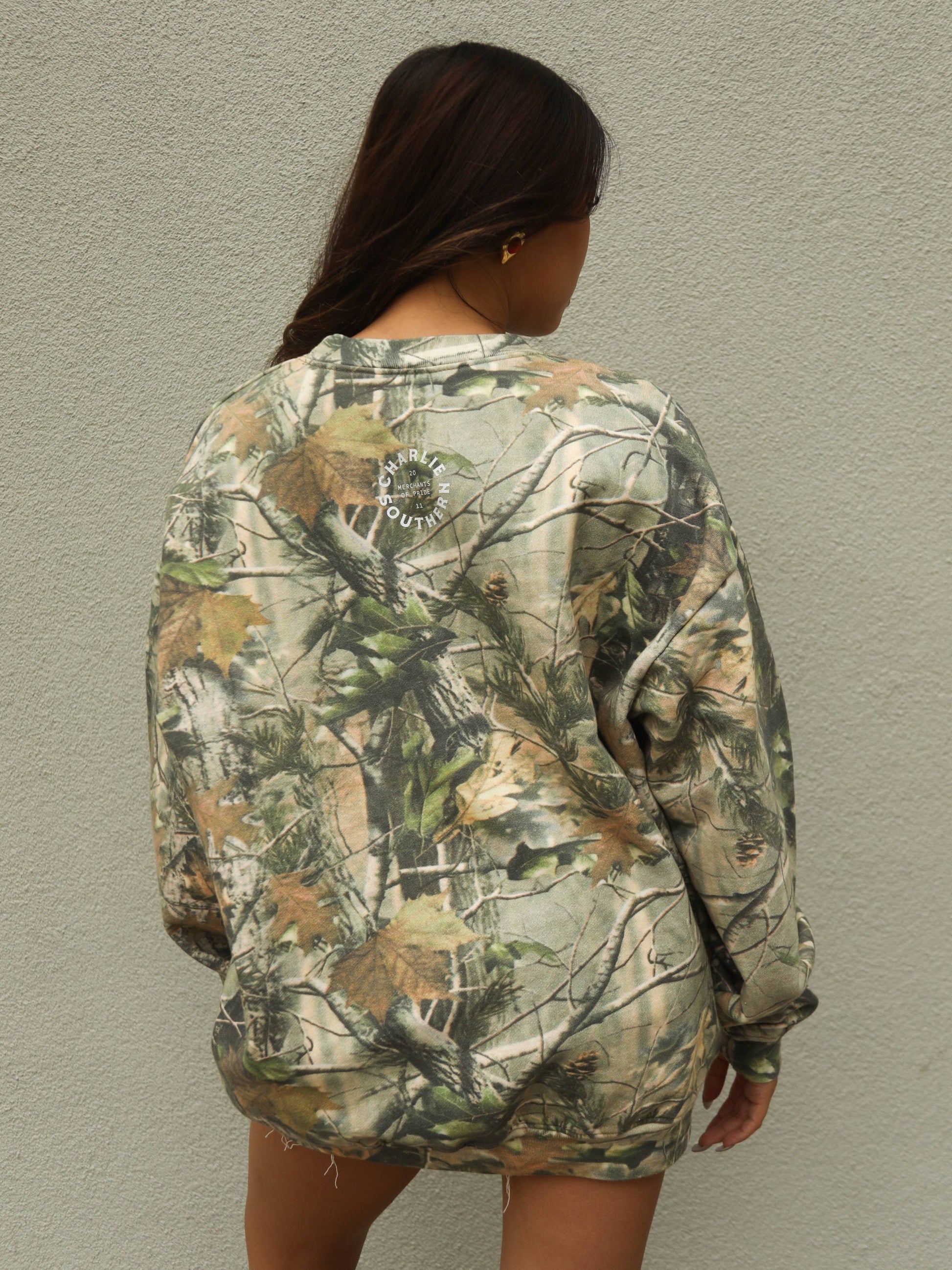 Country inspired oversized sweatshirt with hunting camo print, rodeo graphic design and relaxed styling paired perfectly with denim shorts, trucker cap and cowboy boots