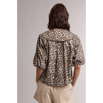 Person wearing a leopard print jacket and beige pants on a plain background