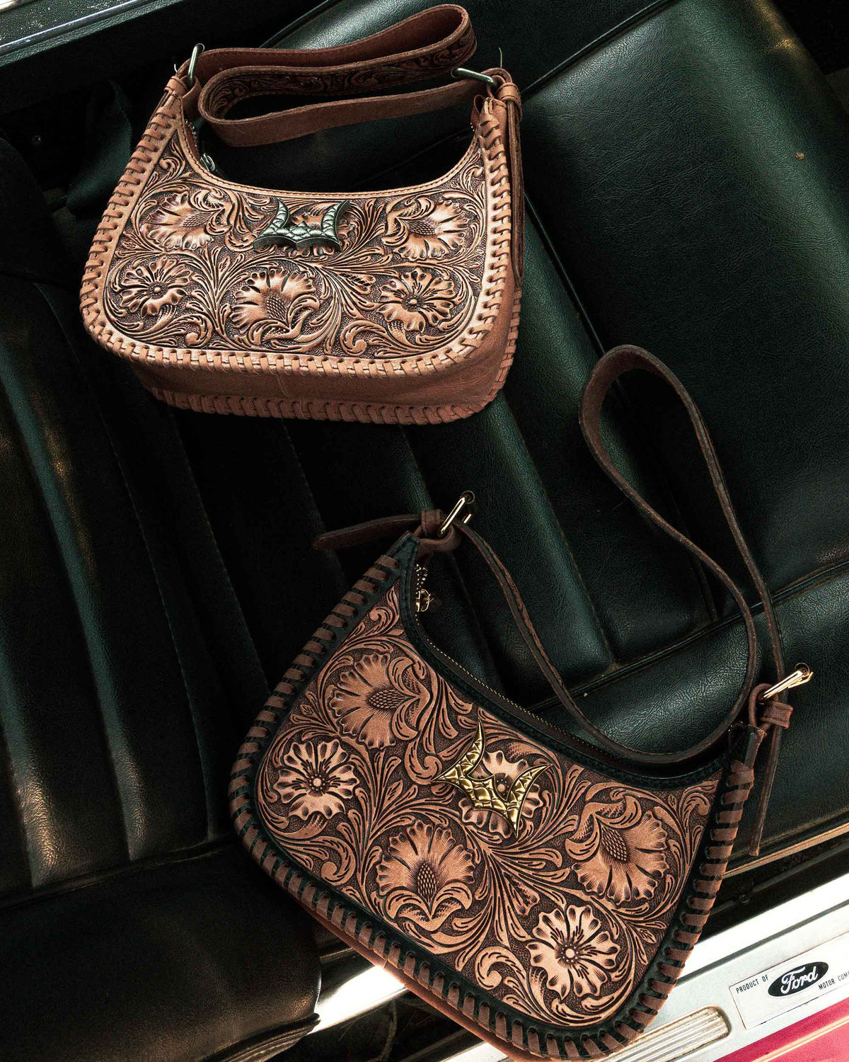 Two brown leather handbags with intricate patterns on a black leather surface.