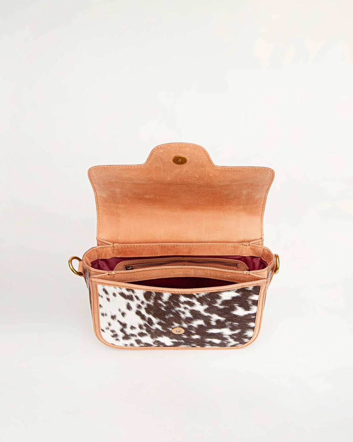 Open tan leather handbag with cowhide pattern interior on a white background