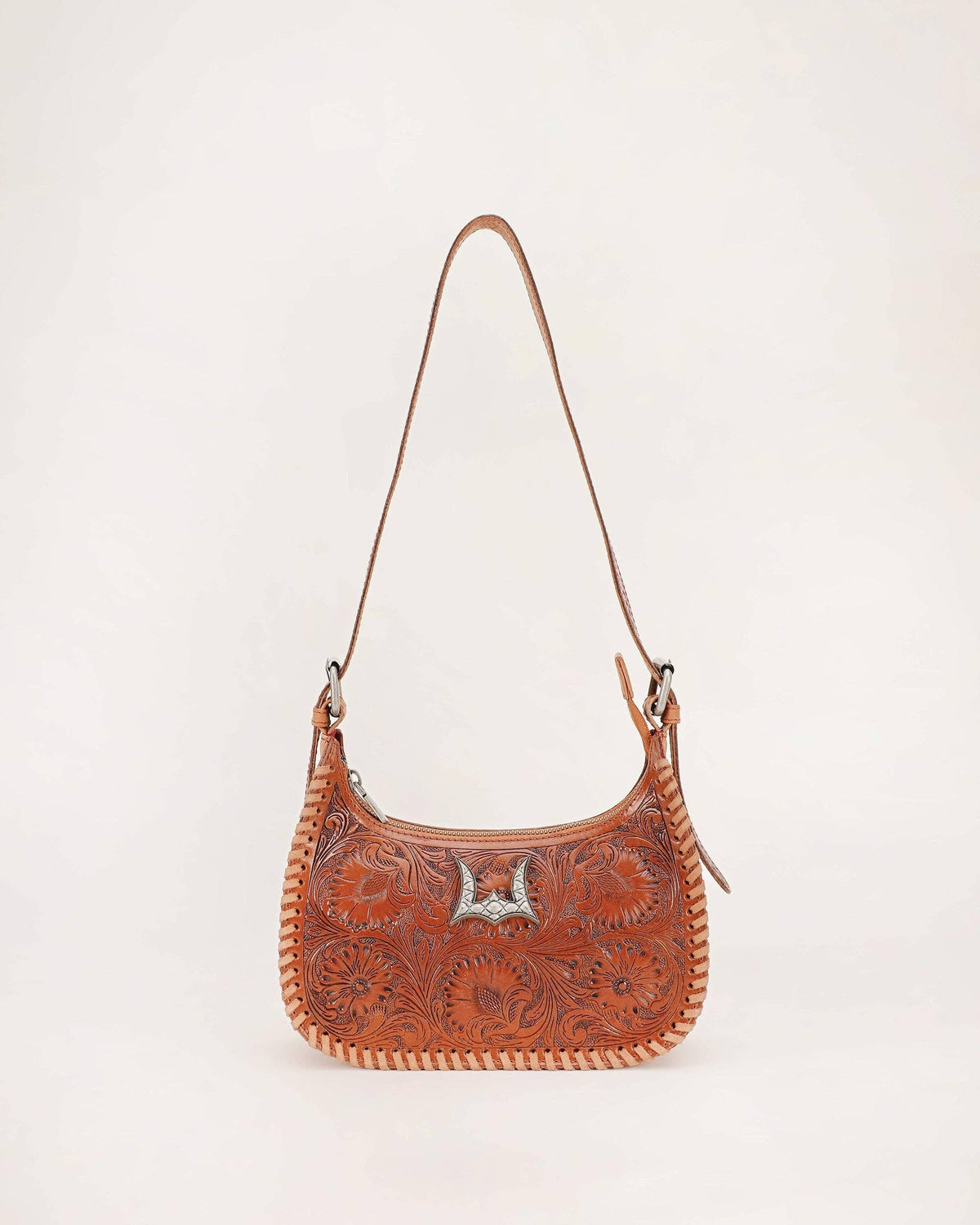 A brown tooled leather shoulder bag with floral embossing, a silver concho accent, and a braided leather trim, shown against a plain white background.