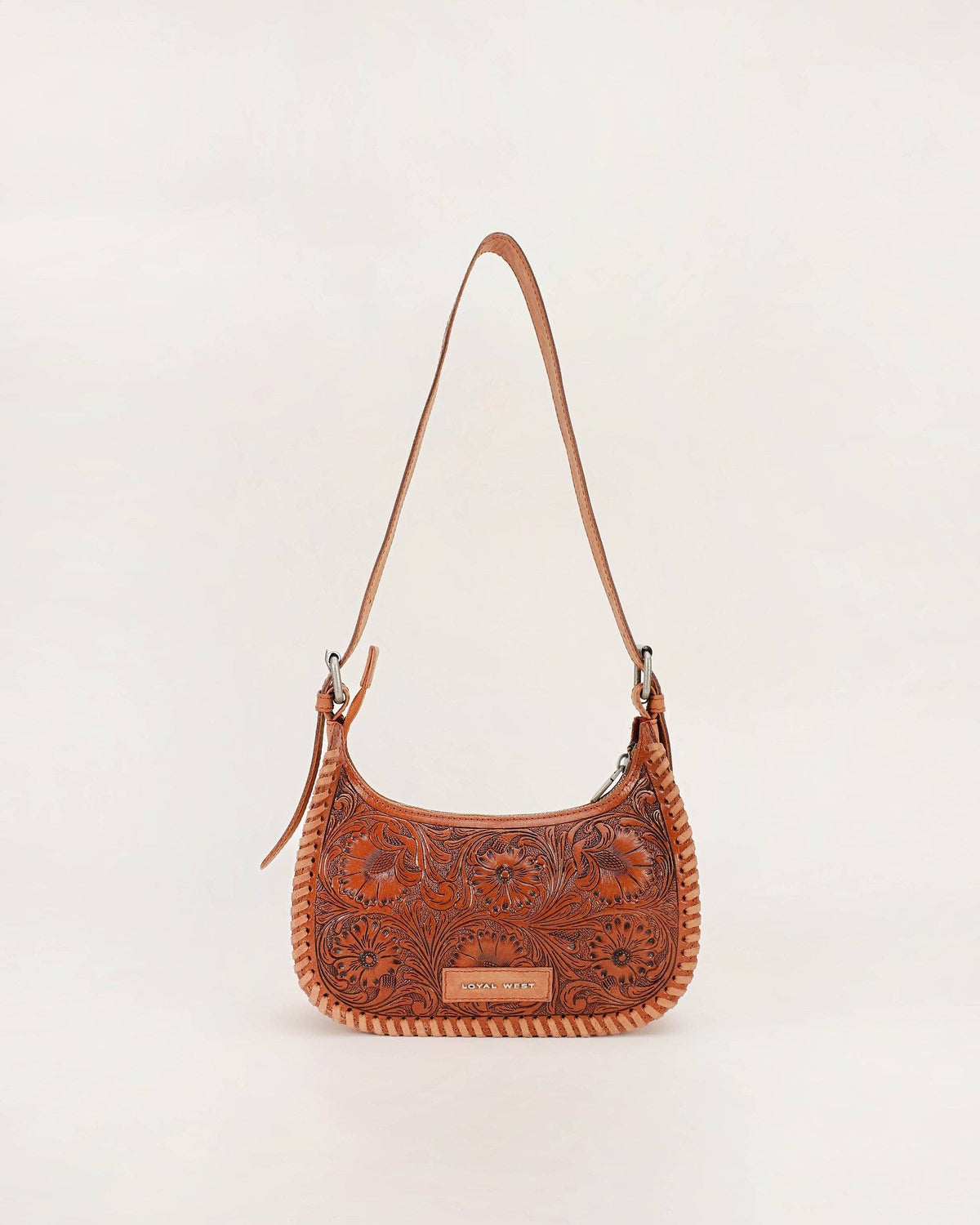 A brown tooled leather shoulder bag with floral embossing, a braided trim, and a long shoulder strap, shown against a plain off-white background.