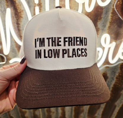 Cream and chocolate brown trucker cap featuring embroidered " I'm The Friend In Low Places" slogan on the front