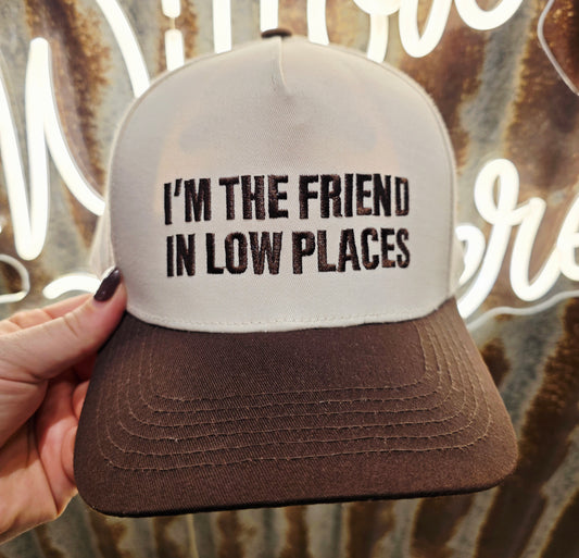 Cream and chocolate brown trucker cap featuring embroidered " I'm The Friend In Low Places" slogan on the front
